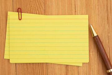 Yellow lined index cards paper with paperclip and pen on wooden desk