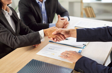 Cropped photo of business people sitting at the desk on workplace in office shaking hands with a...