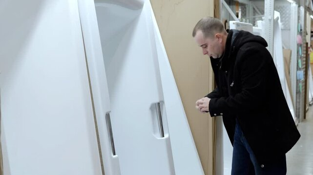 Warehouse customer examines a shower stall, checking its quality and features before making a purchase decision in a home improvement store