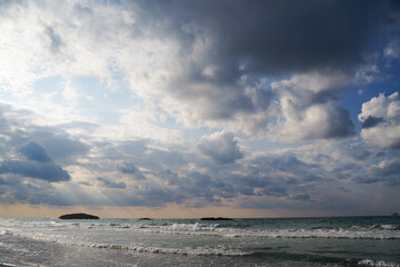Obraz premium Seascape with Waves, small Islands, and sun flares and rays through the Cloudy Sky