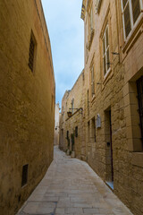 Fototapeta premium Twisting narrow limestone medieval alley with lit lanterns on a moody rainy winter day in Mdina, Malta