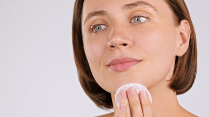 Fototapeta premium Close-up Portrait of happy gorgeous Caucasian woman using Cotton Round on grey backdrop, applying toner, cleansing face, removing makeup. Young woman gently rubs a Cotton Pad on cheek. Facial Cleanser