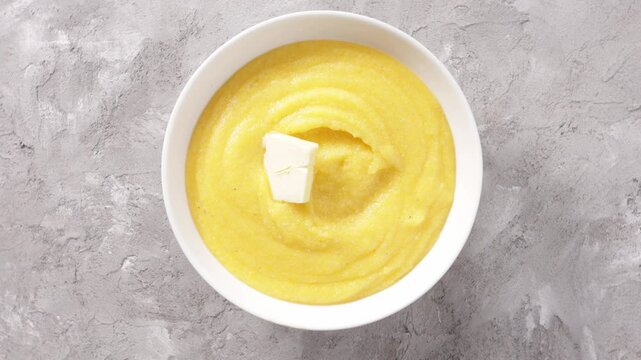 creamy polenta with piece of butter in bowl on light surface rotation food