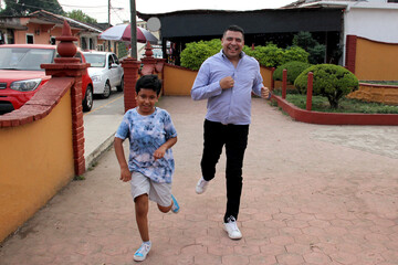 Latino dad and dark-skinned 9-year-old son play a speed race in the street, they have fun and are happy in poverty