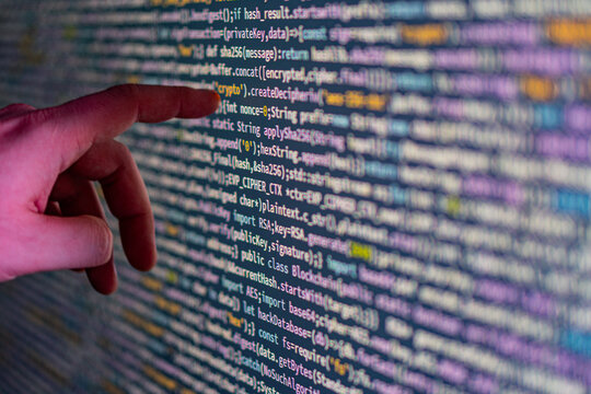 A close-up image of a persons hand pointing at a code display on a large screen, likely in a modern software development workspace or educational setting The hand is wearing a watch