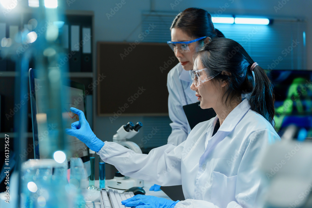 Wall mural two scientists wearing lab coats and safety glasses analyzing data on computer in laboratory at nigh