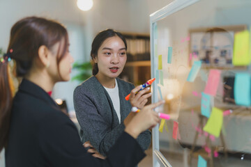 Two businesswomen collaborating on a project, using colorful sticky notes and markers on a whiteboard during a productive meeting in a modern office