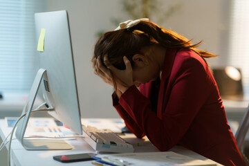 Young businesswoman holding her head in hands, suffering from headache or stress, working on computer in office at night