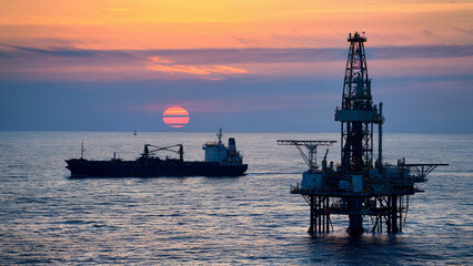 Obraz premium Sunset over ocean; cargo ship and offshore oil rig..