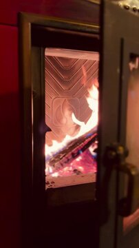 fuoco di legna che arde nel braciere di una vecchia stufa dallo sportello semi aperto