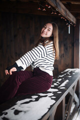 Obraz premium Young girl in striped sweater and corduroy pants sitting and smiling on a snowy bench in winter