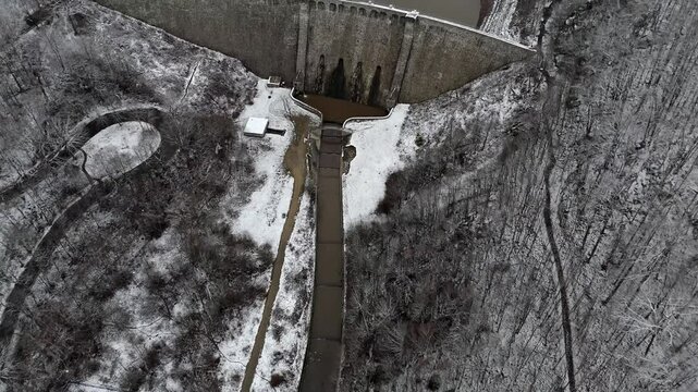 Aerial view reveals a dam and dried lakebed covered in snow. The dark path of a new river highlights the drastic water loss and climate challenges.