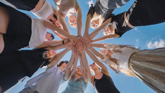 High school students unite in a circle, clasping hands under a vibrant blue sky, representing teamwork, solidarity, and cooperation