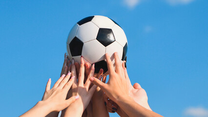 Friends demonstrating teamwork and unity by raising a soccer ball above their heads against a clear blue sky