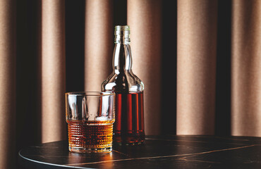 Bourbon, whiskey or scotch in glass with bottle. Lifestyle photo on marble table with textile...