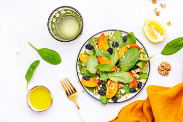 Wintervegan persimmon salad with walnuts, blue raisin and spinach, white background, top view