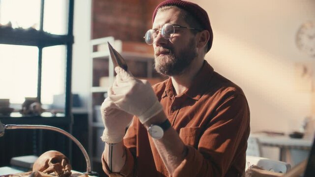 Professional archaeologist in gloves and glasses examining ancient spearhead during research in laboratory