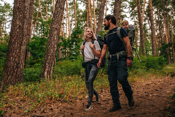 family with a small child in a travel backpack baby carrier. go camping with a tent and backpacks