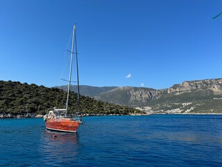 Sailboat anchored in a tranquil lagoon surrounded by hills on a sunny day
