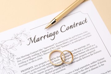 Marriage contract, pen and golden rings on beige background, top view