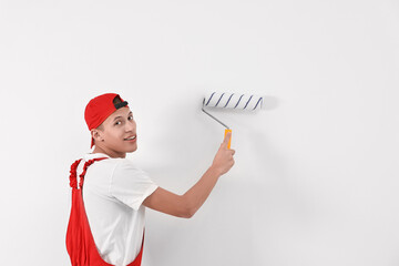 Naklejka premium Smiling handyman painting wall with roller indoors