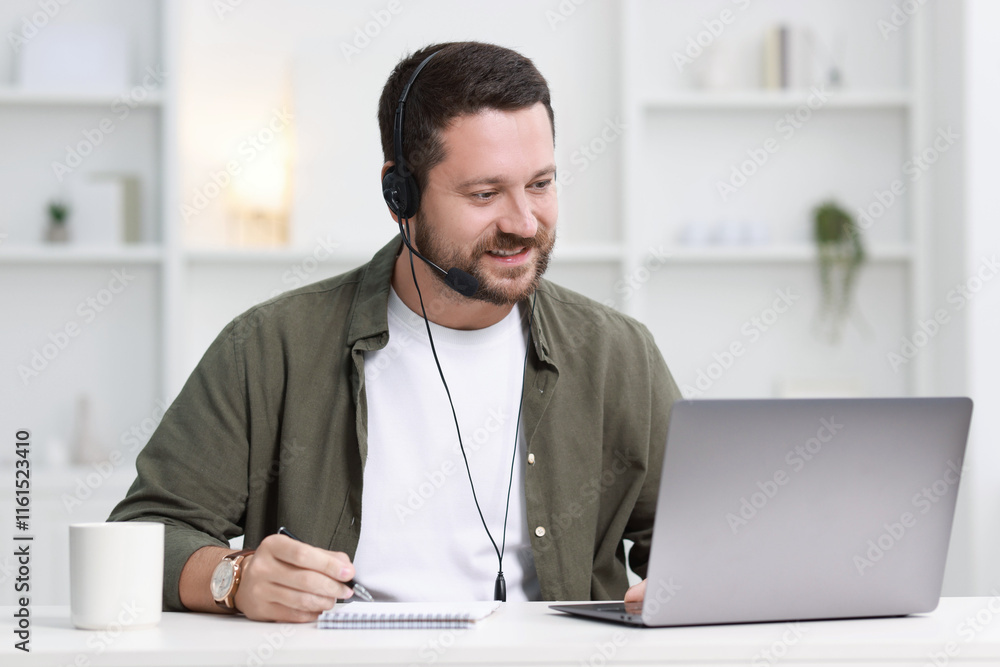 Poster interpreter in headset taking notes while having video chat via laptop at white table indoors