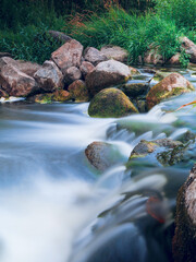 A stream of water flows over rocks and moss. The water is clear and calm, creating a peaceful atmosphere. Fine relaxing nature scene on a small river. Nobody. Motion blur on water surface.