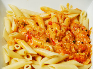 Cooked pasta dish with cheese sauce and herbs in white square plate. Italian style food.