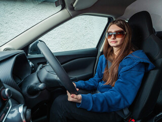A woman is driving a car and looking at the road. She is wearing a blue sweater. Young...