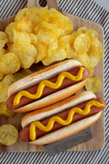 Homemade Boiled Hot Dogs with Mustard and Potato Chips on a Wooden Board, side view. Close-up.