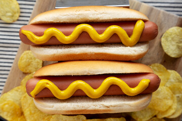 Homemade Boiled Hot Dogs with Mustard and Potato Chips on a Wooden Board, top view. Flat lay, overhead, from above.