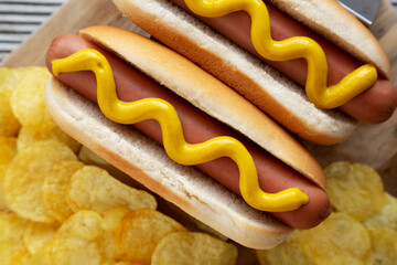 Homemade Boiled Hot Dogs with Mustard and Potato Chips on a Wooden Board, top view. Flat lay, overhead, from above.