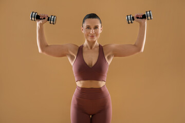 Woman exercising with dumbbells on beige background