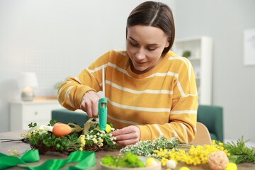 Woman with hot glue gun making craft at table indoors