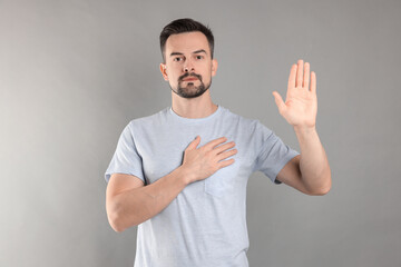 Man making promise with raised hand on grey background. Oath gesture