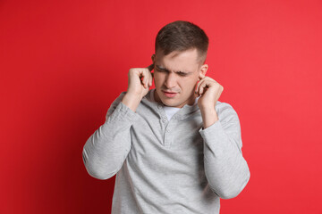 Man covering his ears with fingers on red background