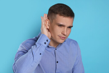 Man showing hand to ear gesture on light blue background