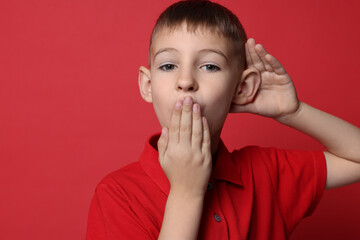 Little boy showing hand to ear gesture on red background