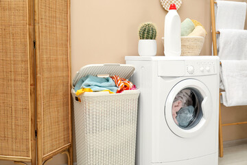 Wicker basket full of laundry, washing machine and detergent in bathroom
