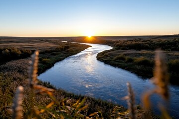A stunning sunset illuminates a winding river, surrounded by lush fields, creating a picturesque scene that embodies the beauty and tranquility of nature's landscapes.