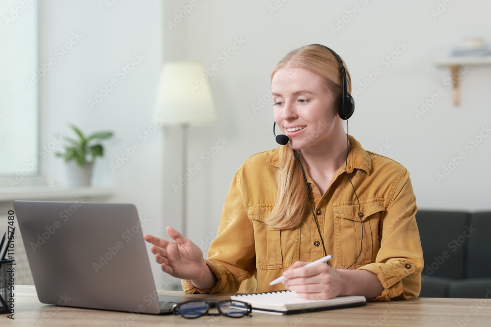 Poster interpreter in headset taking notes while having video chat via laptop at table indoors