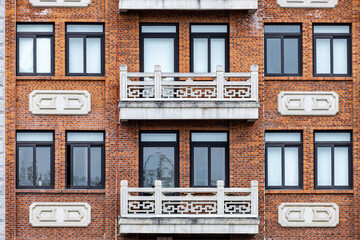 Obraz premium The symmetrical facade of a classic brick apartment building with distinctive white stone balconies featuring ornate geometric railings. Facade of a new architecture