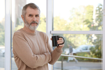 Mature man with cup of hot drink at home. Space for text