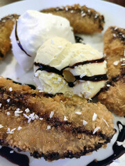 A plated dessert featuring crispy fried bananas drizzled with chocolate sauce, served alongside scoops of vanilla ice cream and whipped cream