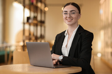 Woman in stylish formal suit working on laptop at table indoors