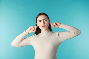 Frustrated woman covering her ears from loud noise on blue background