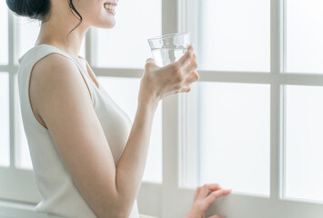家で水・ミネラルウォーター・白湯をコップで飲むリラックスした女性

