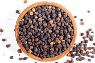 Black peppercorns (black pepper) in a wooden bowl isolated on a white background