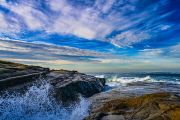 2023-12-31 THE ROCKY SHORELINE IN LA JOLLA CALIFORNIA WITH WAVES HITTING THE ROCKS SPLASHING WITH A NICE INTENSE SKY NEAR SAN DIEGO CALIFORNIA