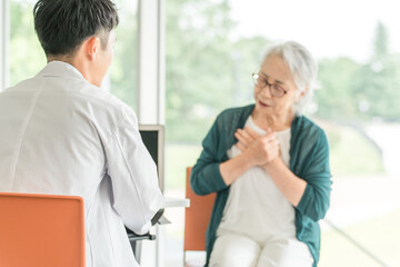 Obraz premium 病院・介護施設で医師に病状を伝えるシニア女性を問診する男性医師（診療・診察・人間ドック・健康診断） 